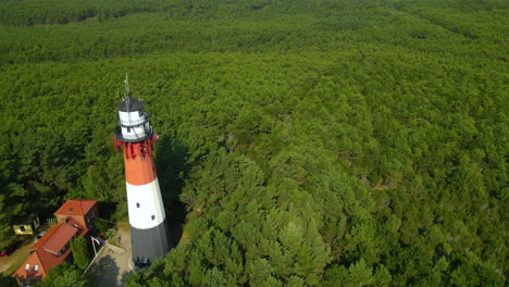 The-drone-slow-pulls-out-and-reveals-Stilo-Lighthouse-and-green-forest-around-it---lighthouse-located-in-Osetnik-on-the-Polish-coast-of-the-Baltic-Sea,-close-to-the-village-of-Sasino,-aerial-close-up