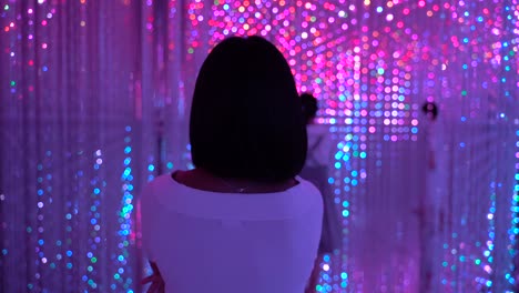 Following-back-of-female-walking-through-colorful-neon-lights-at-art-exhibition