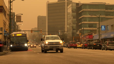 Downtown-Vancouver-Under-Orange-Sky-Due-To-Wildfire-Smoke---City-Bus-Arrived-At-The-Bus-Stop-With-Cars-Driving-On-The-Road-In-The-Morning-At-The-West-Broadway-Near-Cambie-Street-In-BC,-Canada