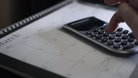 Hands-using-calculator-on-March-calendar-medium-panning-shot