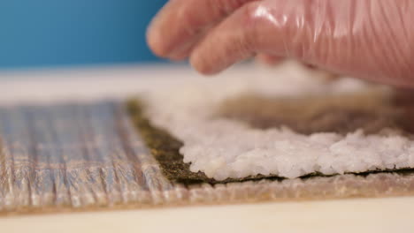 Hands-With-Disposable-Plastic-Gloves-Flattening-Sushi-Rice-On-Seaweed-Wrap---close-up