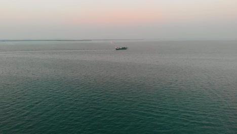 Drohne,-Die-über-Dem-Persischen-Golf-Aufsteigt,-Während-Ein-Frachtschiff-Bei-Sonnenuntergang-Vorbeifährt