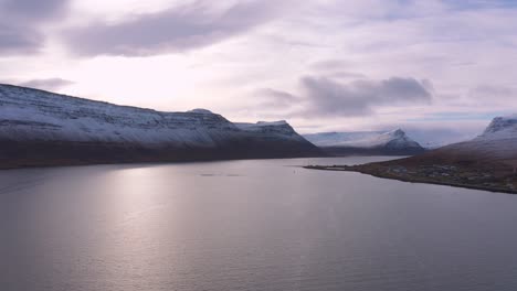 Vista-Aérea-Que-Muestra-Un-Sereno-Océano-ártico-Rodeado-De-Montañas-Cubiertas-De-Nieve-En-Un-Hermoso-Día-Nublado-Durante-Los-Inviernos-Extremos,-Fiordos-Occidentales-Islandeses