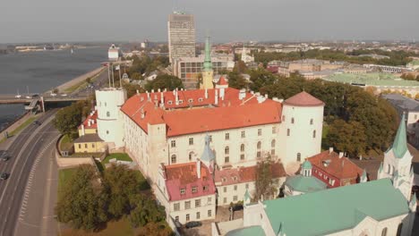 Aerial-drone-flying-above-Riga-Castle-by-Daugava-River,-Latvia,-day