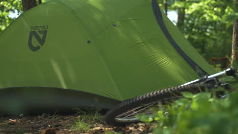 A-bright-green-Nemo-tent-sits-in-the-middle-of-a-sunny-wooded-forest-next-to-mountain-bike-during-a-summer-camping-trip