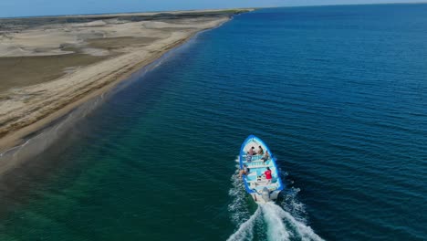 Aerial-view-Tilting-up-shot,-Tourist-boat-moving-along-the-coastline-of-La-Purisima-Baja-California-sur,-Mexico,-bright-blue-sky-in-the-background