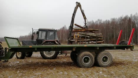 Log-Loader-Loading-Logs-Into-Flatbed-Truck-In-Forest-On-Winter-Day-With-Snow-Falling---wide-shot