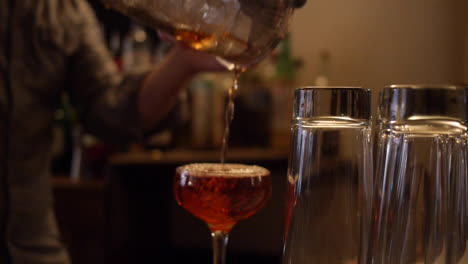 Bartender-Pours-Whiskey-Manhattan-Cocktail-Into-Glass-on-Bar