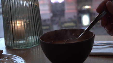 Close-up-of-a-male-hand-stirring-a-black-bowl-of-hot-tomato-soup-with-a-metal-spoon