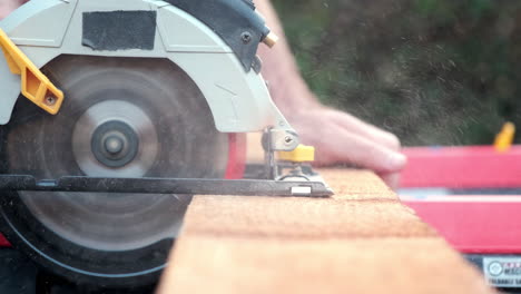 Close-Up-Slow-Motion-Shot-of-Electric-Power-Saw-Slicing-Through-Plank-of-Wood-Outside