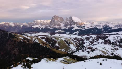 Panoramic-backwards-aerial-view-of-snow-covered-Dolomites-mountain-range-from-Seiser-Alm---Alpe-di-Siusi-plateau-in-South-Tyrol,-Italy-around-sunset