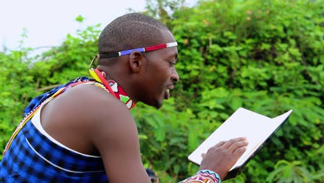 African-man,-laughing-while-reading-a-book,-in-jungle,-wearing-tribal-gear