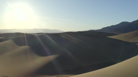 Drone-footage-flying-towards-man-walking-along-sand-dunes-in-the-desert,-with-soft-light-and-golden-dunes-at-sunset