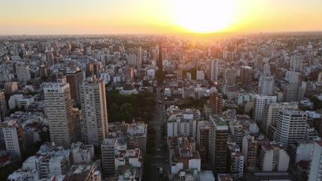 Dolly-in-flying-over-Belgrano-neighborhood-tall-buildings-at-sunset-with-shiny-sun-in-background,-Buenos-Aires,-Argentina