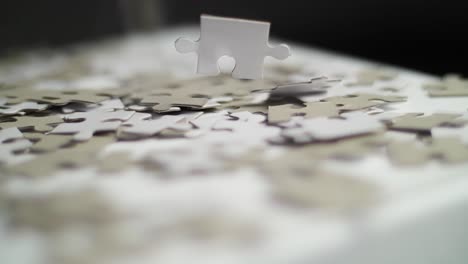 Close-up-of-white-and-gray-puzzle-pieces-falling-in-slow-motion-on-a-white-surface-and-bouncing-off-with-a-dark-background