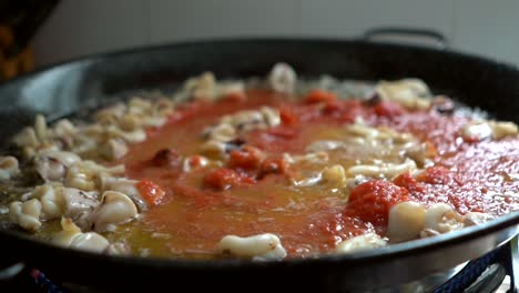 adding-crushed-tomato-to-fry-during-the-preparation-of-fideua-in-paellon-typical-Spanish-food