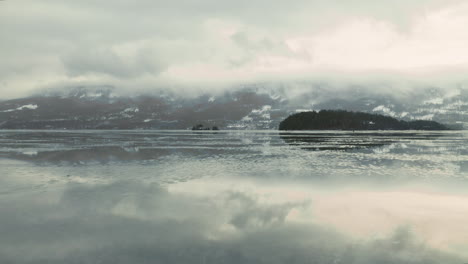 Traveling-across-the-frozen-lake-of-Haugastol,-Norway-in-winter--low-aerial