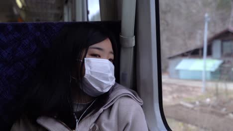 Trauriges-Asiatisches-Mädchen-Mit-Gesichtsmaske,-Das-Aus-Dem-Zugfenster-Auf-Die-Landschaft-Blickt