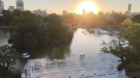 Aerial-dolly-in-over-white-bridge-and-boats-sailing-in-pond-at-Rosedal-gardens-at-golden-hour,-Buenos-Aires