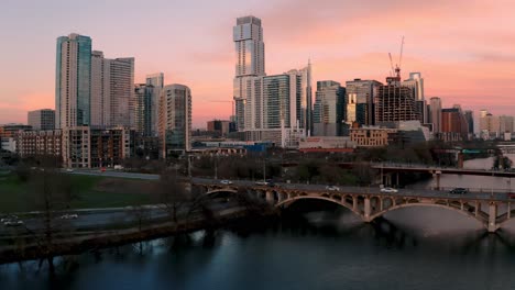 Downtown-Austin-Texas-Skyline-4k-aerial-orbit-over-Lamar-Pedestrian-Bridge,-traffic-and-Ladybird-Lake-at-sunset