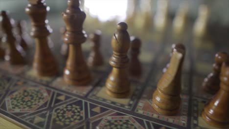Close-up-pan-shot-of-retro-wooden-figures-of-chessboard-and-sunlight-in-backdrop
