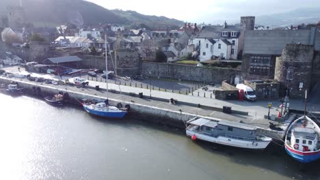 Idyllic-Conwy-castle-and-harbour-fishing-town-boats-on-coastal-waterfront-aerial-low-pull-away-right