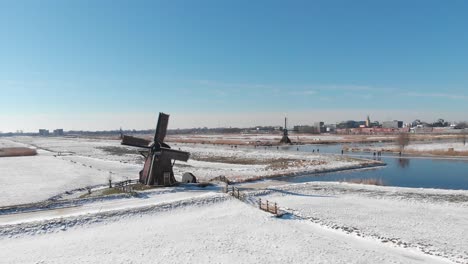 Ice-skaters-on-frozen-canal-beside-Netherlands-windmill,-winter-aerial-view