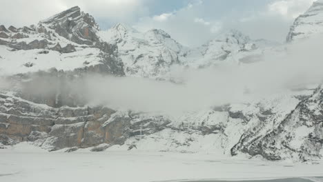 Una-Gruesa-Capa-De-Niebla-Cuelga-Frente-A-Una-Montaña-Cubierta-De-Nieve