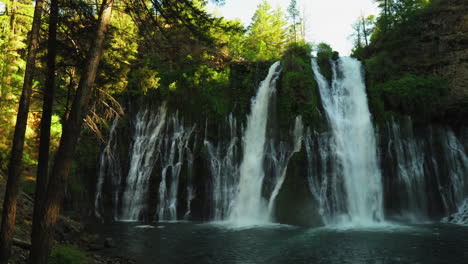 Panning-view-of-Burney-Falls,-forest-waterfall-in-California,-with-water-falling-down-a-cliff