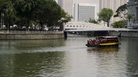 Traditionelles-Touristenboot,-Das-Entlang-Des-Singapur-Flusses-In-Richtung-Cavenagh-Bridge-Segelt---Weitschuss