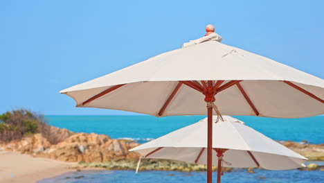 Close-up-of-beach-parasols,-umbrella-sunshades-and-tropical-sea-on-summer-breeze