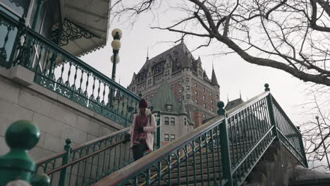 Smiling-Woman-Walking-Down-The-Stairs-In-Front-Of-Chateau-Frontenac-in-Quebec-City,-Canada---high-angle-shot