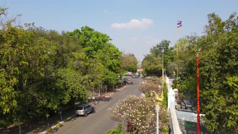 Wat-Phra-Phutthabat,-Saraburi,-Thailand,-a-steady-aerial-4K-footage-of-a-community,-entrance-into-the-Buddhist-temple,-a-Thai-flag,-street-lights,-people-crossing,-cars-and-motorcycles-passing