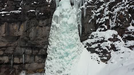 Luftaufnahme-Des-Gefrorenen-Eisigen-Wasserfalls-Und-Der-Schneebedeckten-Klippe-In-Der-Berglandschaft,-Dolly-Drohnenaufnahme