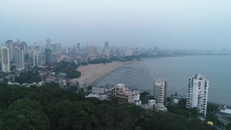 A-cinematic-drone-shot-of-the-famous-Marine-Drive-Chaupati-Beach-point-in-South-Bombay-region-of-Mumbai-City,-overlooking-the-hanging-garden-hill-and-forest-in-a-slow-smooth-motion