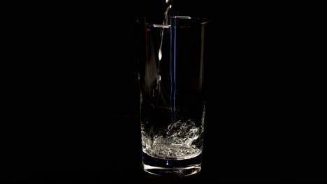 Pouring-water-into-a-glass-against-black-background-slow-motion