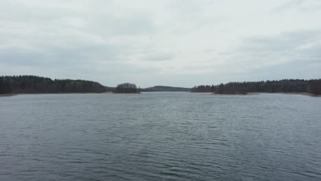 AERIAL:-Rippling-Water-on-the-Surface-of-Lake-with-Forest-in-the-Background-and-Gloomy-Sky-in-Horizon