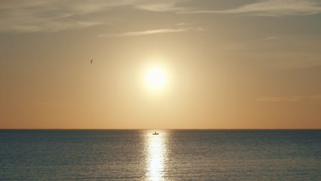 Lonely-boat-sits-at-sea-during-sunset-in-sun's-reflection,-long-shot