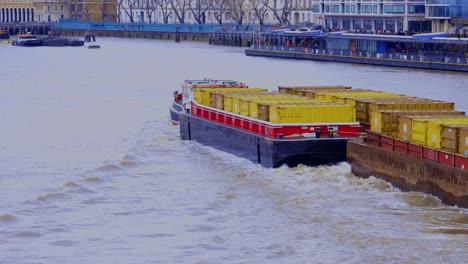A-small-tug-boat-towing-three-barges-full-of-containers-under-the-Tower-bridge-and-up-the-Thames-River-in-London