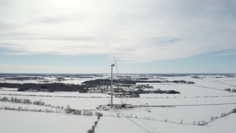 Giant-windmill-under-construction-in-winter-with-snowy-landscape-and-tall-orange-crane
