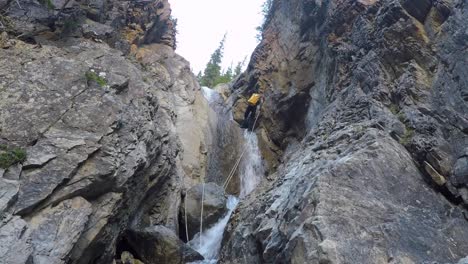 Man-in-wetsuit-rappels-river-canyon-waterfall-with-pack-on-his-back