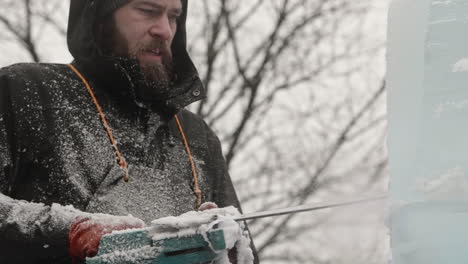 Ice-sculptor-staring-intently-at-ice-blocks-as-he-uses-electric-chainsaw-to-carve,-Slow-Motion