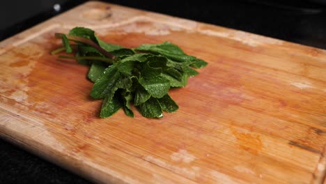 Dropping-fresh-juicy-peppermint-leaves-on-a-wooden-chopping-board,-slow-motion