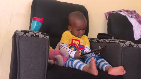 A-young-African-boy-plays-on-a-tablet-computer,-while-sitting-in-a-chair-in-his-home