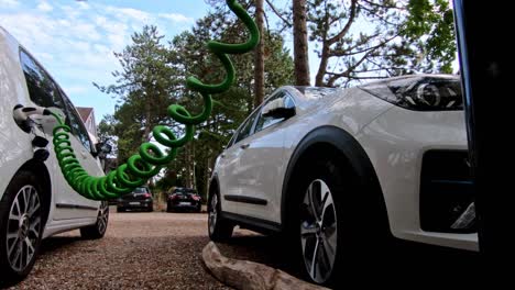 Two-white-ev-cars-plugged-into-a-public-charging-station-in-a-forest