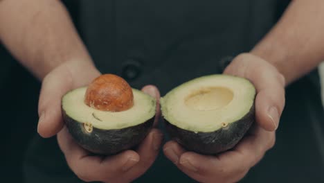 Close-up-of-male-hands-opening-avocado-fruit-in-half-with-brown-seed-inside