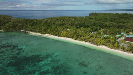 Aerial-view-of-houses,-forest-and-a-beach,-on-the-Lifou-island---pan,-drone-shot
