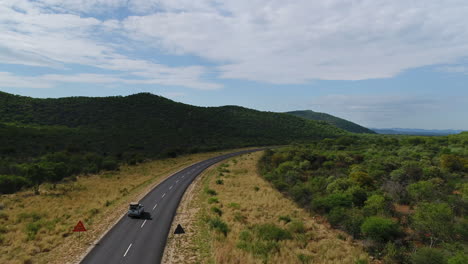 Aerial-of-4x4-truck-driving-in-Namibia-on-a-empty-road-surrounded-with-green-forest