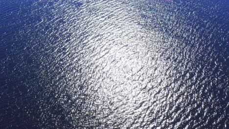 Drone-shot-of-sunlight-glimmering-on-a-wavy-blue-water-surface