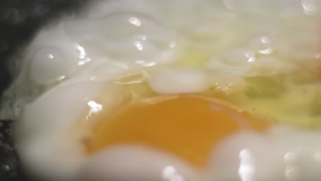 Frying-eggs-for-breakfast-in-a-black-iron-pan-with-bubbles-jumping-in-hot-oil-as-a-soft-background-with-bokeh